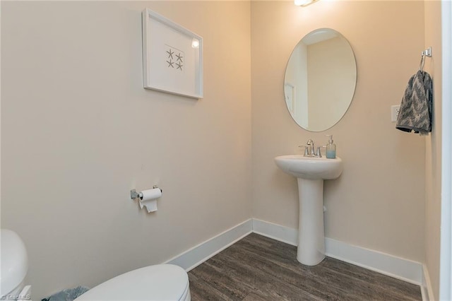 half bath with baseboards, toilet, and wood finished floors