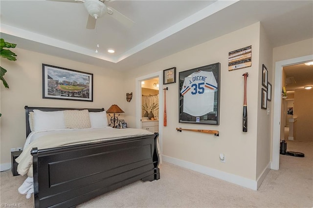 bedroom featuring ceiling fan, baseboards, light carpet, ensuite bath, and a raised ceiling