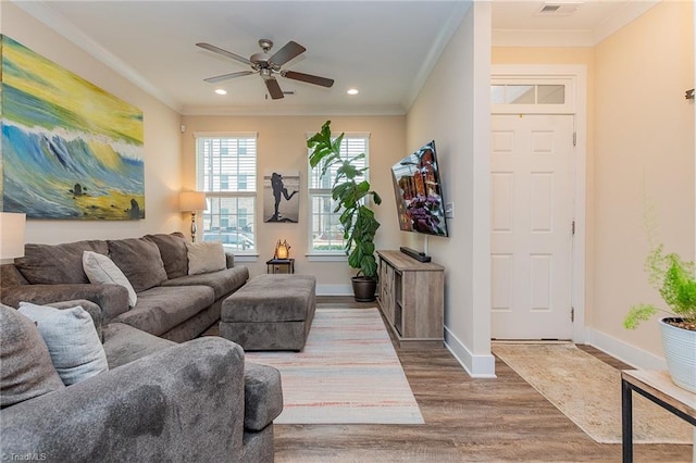 living room with wood finished floors, visible vents, baseboards, ceiling fan, and ornamental molding