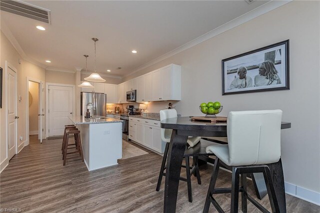 kitchen featuring a breakfast bar area, visible vents, an island with sink, white cabinets, and appliances with stainless steel finishes