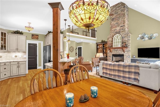 7821 Charles Place Dr, Kernersville, NC 27284 - dining space with light wood-style flooring, high vaulted ceiling, a stone fireplace, and decorative columns