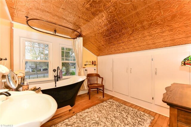 bathroom with a bathtub, vaulted ceiling, and hardwood / wood-style flooring