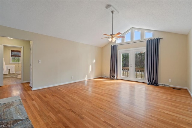 unfurnished living room with a wealth of natural light, french doors, vaulted ceiling, and light wood-style flooring