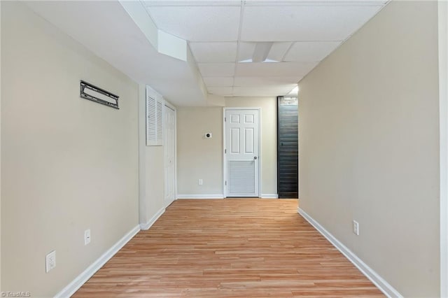 spare room featuring light wood-type flooring, a drop ceiling, and baseboards