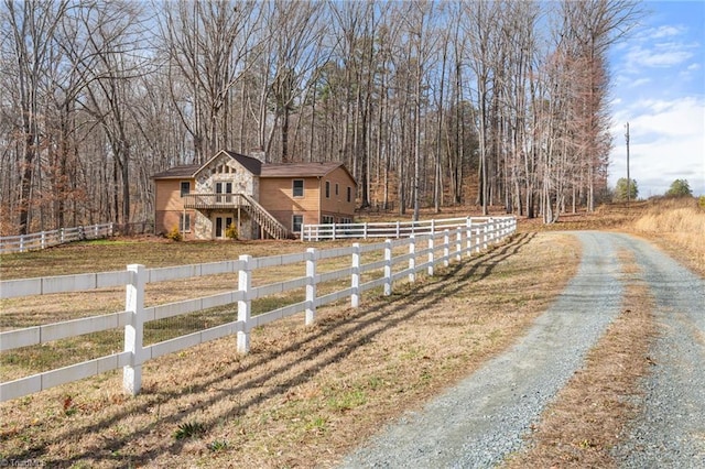 view of front of home featuring a fenced front yard, driveway, a wooded view, and stairs