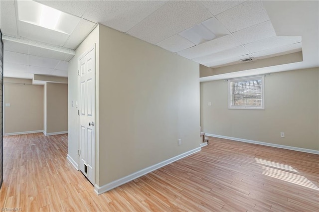 unfurnished room featuring baseboards, light wood-style flooring, visible vents, and a drop ceiling