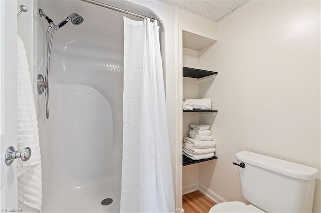 bathroom with a drop ceiling, toilet, wood finished floors, baseboards, and a stall shower