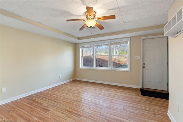 spare room featuring light wood-type flooring, a ceiling fan, baseboards, and a paneled ceiling