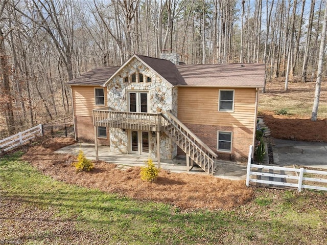 view of front of home featuring stone siding, fence private yard, stairs, french doors, and a patio area