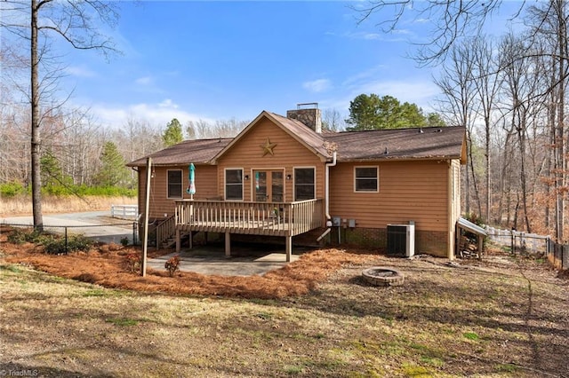 rear view of property with a deck, an outdoor fire pit, central AC, fence, and a chimney