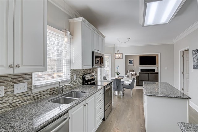 kitchen featuring light wood finished floors, dark stone counters, ornamental molding, a sink, and appliances with stainless steel finishes