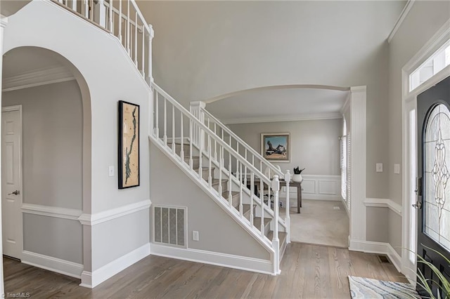 entrance foyer with visible vents, crown molding, a towering ceiling, wood finished floors, and arched walkways