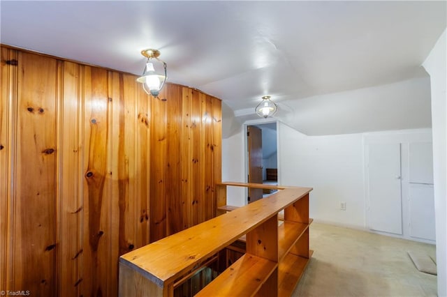 hall featuring light carpet, wooden walls, and lofted ceiling