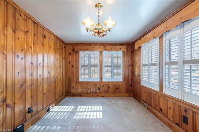 empty room with light carpet, ornamental molding, wooden walls, and a notable chandelier