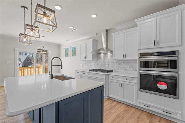 271 Redland Rd, Advance, NC 27006 - kitchen featuring wall chimney range hood, stainless steel appliances, light wood-style flooring, tasteful backsplash, and light countertops