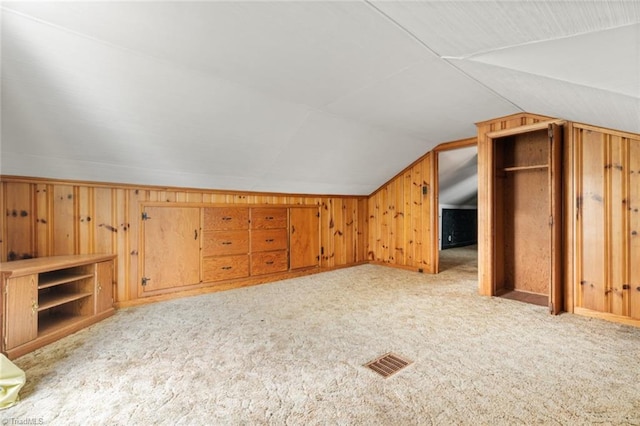 bonus room with lofted ceiling, wooden walls, and light colored carpet