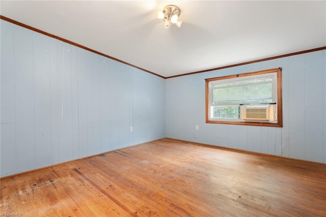 spare room with light wood-type flooring, wood walls, and crown molding