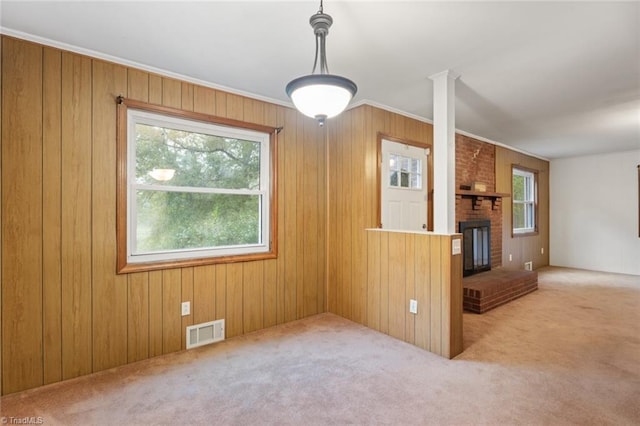 unfurnished living room with a healthy amount of sunlight, a fireplace, wooden walls, and light carpet