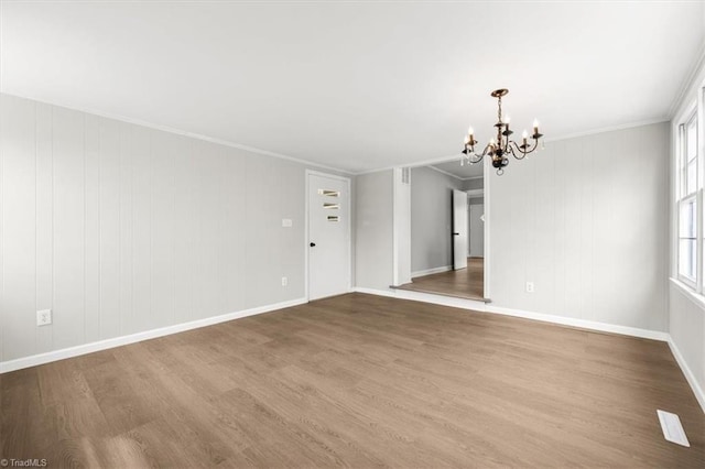 empty room with wood-type flooring, ornamental molding, and a chandelier