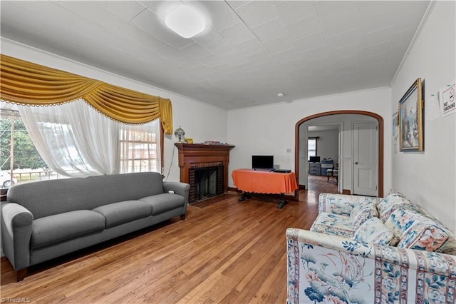 living room with a brick fireplace, ornamental molding, and hardwood / wood-style flooring