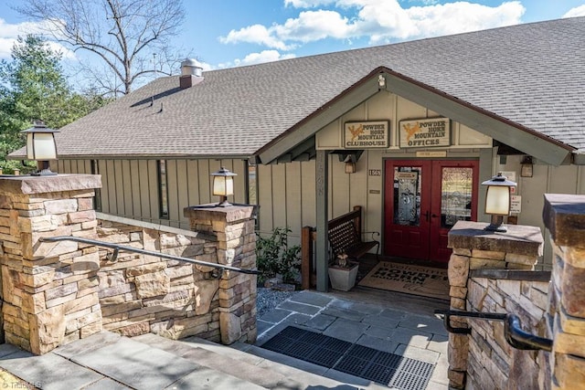 view of exterior entry with french doors, roof with shingles, and board and batten siding