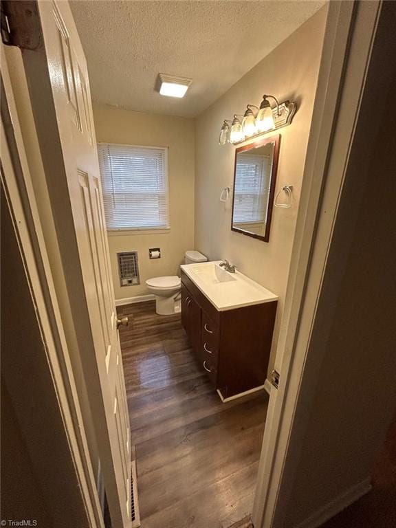 bathroom featuring hardwood / wood-style flooring, vanity, heating unit, a textured ceiling, and toilet