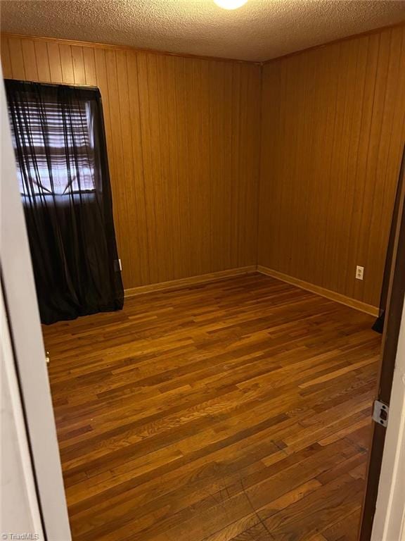 empty room with dark hardwood / wood-style floors, elevator, a textured ceiling, and wooden walls