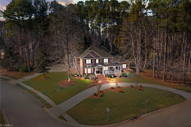 view of front of house featuring covered porch, curved driveway, and a front lawn
