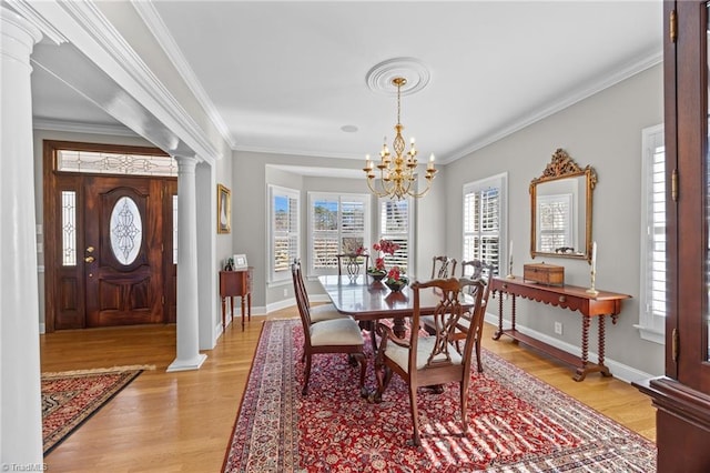 dining room with a notable chandelier, baseboards, crown molding, light wood-style floors, and ornate columns