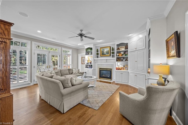 living room featuring ceiling fan, ornamental molding, a fireplace with flush hearth, and light wood-style flooring