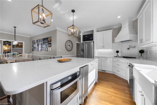 kitchen with white cabinets, appliances with stainless steel finishes, custom exhaust hood, and a notable chandelier
