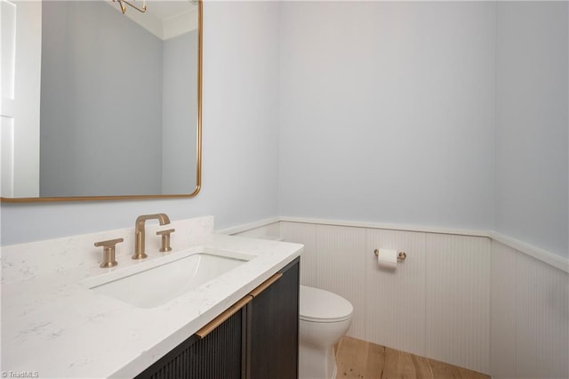 half bath featuring toilet, wainscoting, wood finished floors, and vanity