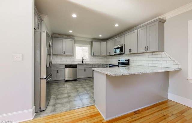 kitchen with kitchen peninsula, light stone counters, stainless steel appliances, sink, and gray cabinets