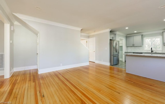 unfurnished living room with light hardwood / wood-style floors, crown molding, and sink