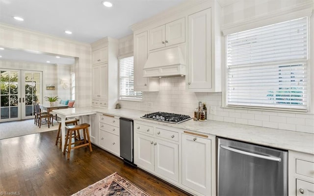 kitchen with white cabinets, custom range hood, stainless steel appliances, and light stone counters