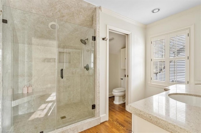 bathroom with hardwood / wood-style flooring, toilet, an enclosed shower, and ornamental molding