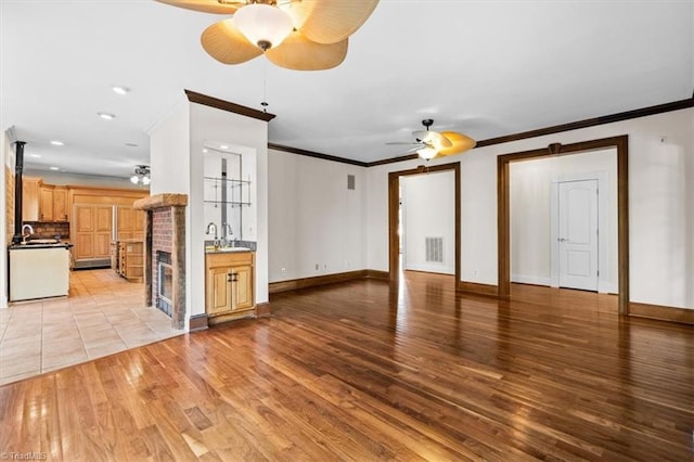 unfurnished living room featuring sink, a fireplace, crown molding, and light hardwood / wood-style flooring