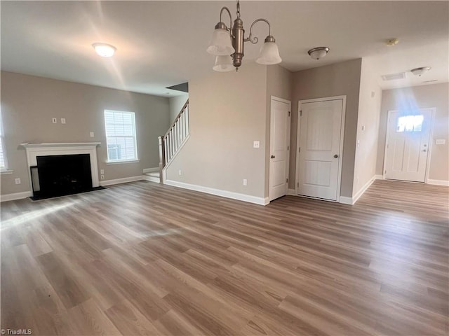 unfurnished living room featuring stairs, baseboards, a fireplace, and wood finished floors