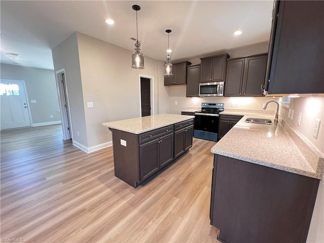 kitchen with light wood-style flooring, a kitchen island, a sink, appliances with stainless steel finishes, and light stone countertops