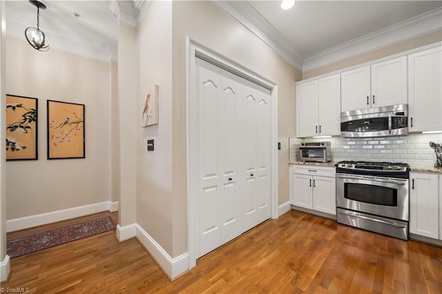 kitchen featuring backsplash, ornamental molding, stainless steel appliances, light wood-style floors, and white cabinetry