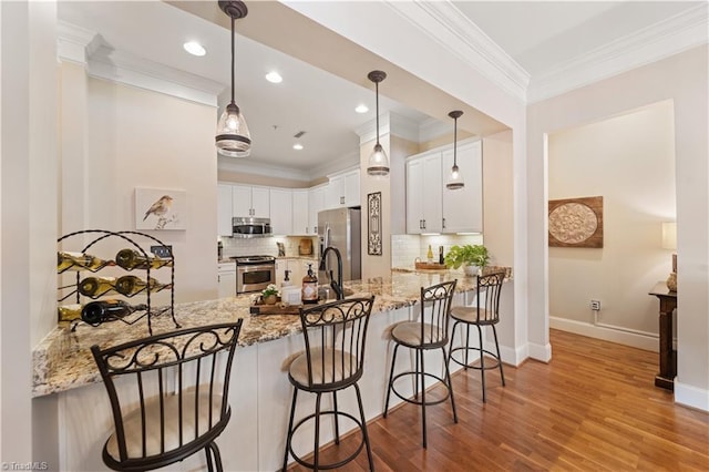 kitchen featuring a peninsula, light stone countertops, appliances with stainless steel finishes, and ornamental molding