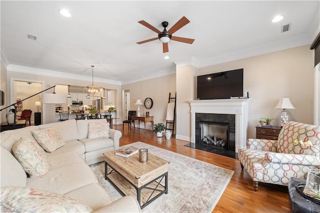 living room with wood finished floors, visible vents, a fireplace, recessed lighting, and ornamental molding