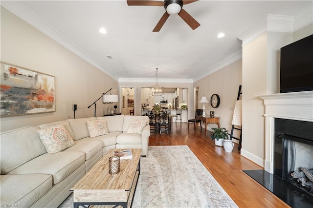 living area with a fireplace with raised hearth, ornamental molding, wood finished floors, baseboards, and ceiling fan