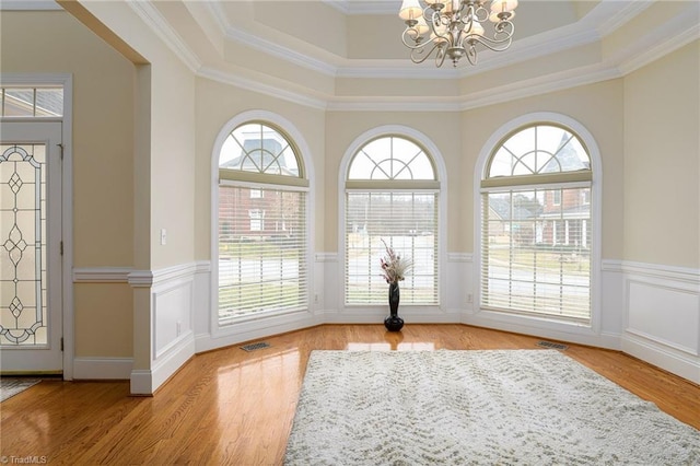 interior space with ornamental molding, a raised ceiling, light wood-type flooring, and a notable chandelier