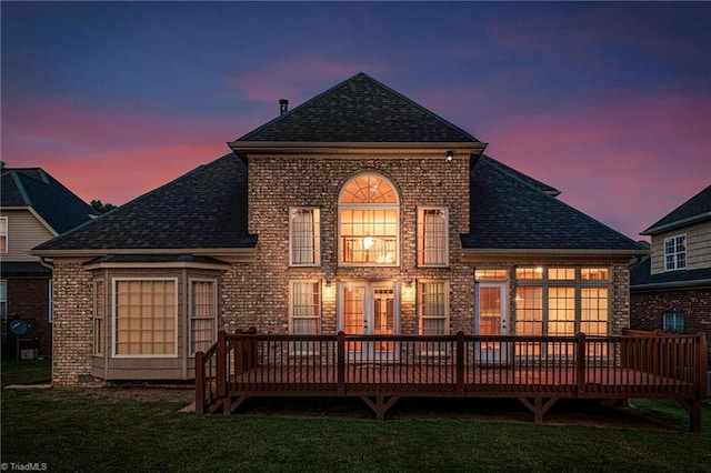 back house at dusk featuring a wooden deck and a yard