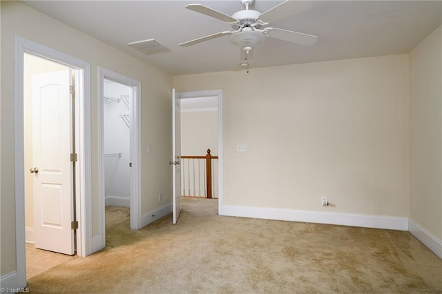 unfurnished bedroom with ceiling fan, a walk in closet, a closet, and light carpet