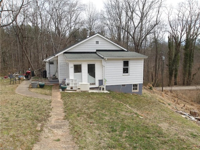 view of front of house featuring entry steps, a front yard, a view of trees, and a shingled roof