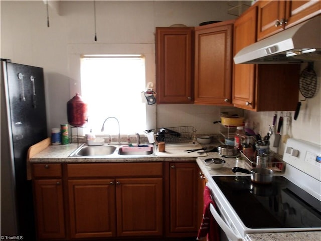 kitchen with under cabinet range hood, light countertops, freestanding refrigerator, white electric range, and a sink