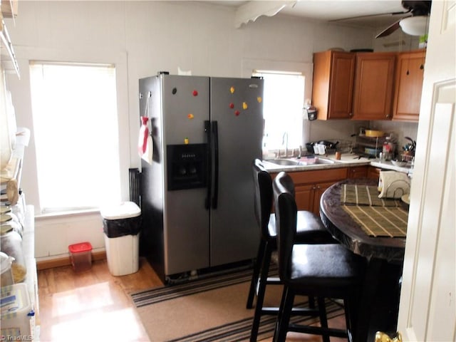 kitchen with light wood-type flooring, a ceiling fan, a sink, stainless steel fridge, and brown cabinetry