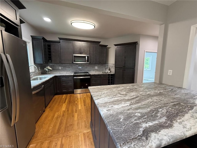 kitchen with appliances with stainless steel finishes, a sink, light wood-style floors, backsplash, and light stone countertops